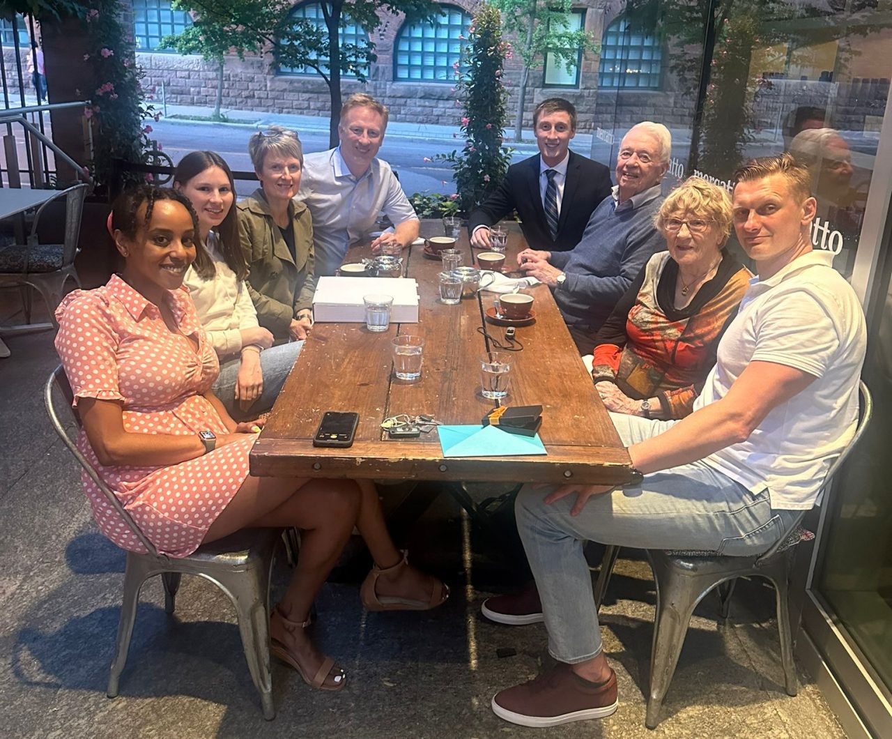 A group of people sitting at an outdoor table in a courtyard with glasses of water and tea cups after dinner.