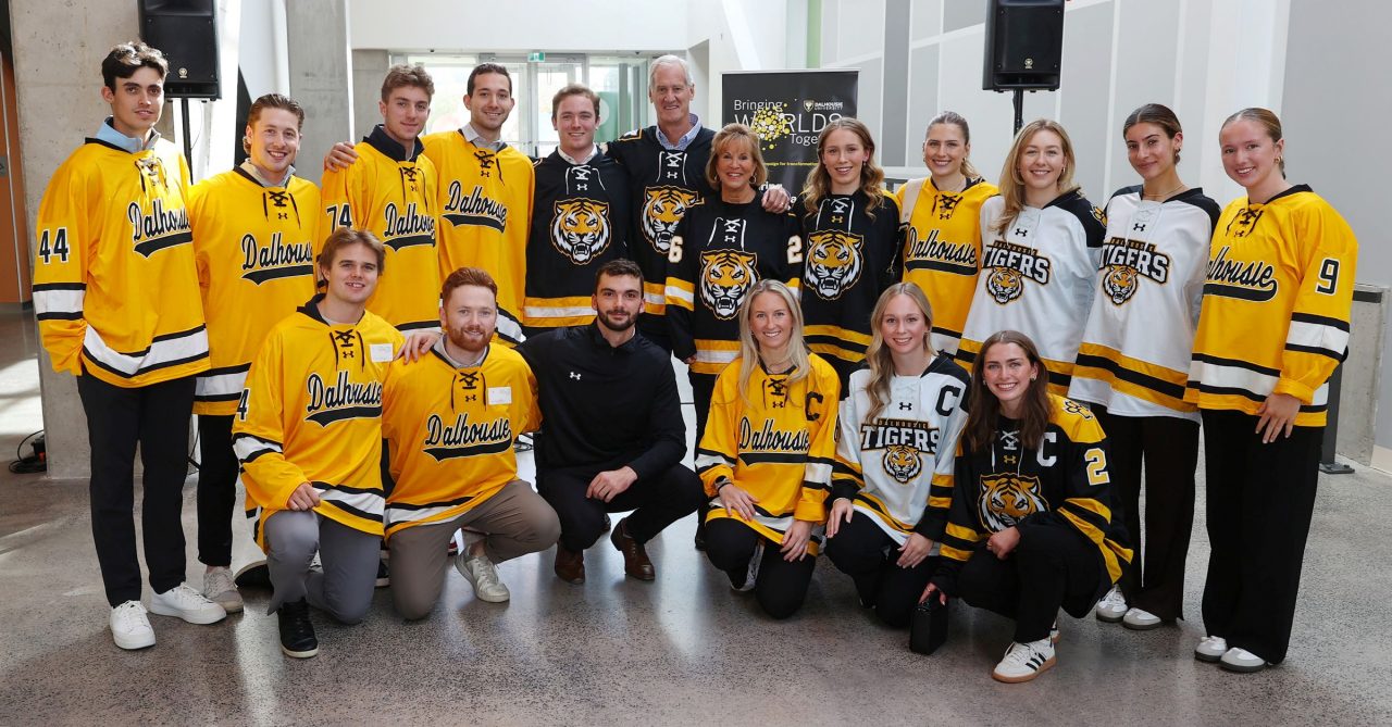 A group of people wearing black, white and gold hockey jerseys grouped together, smiling.