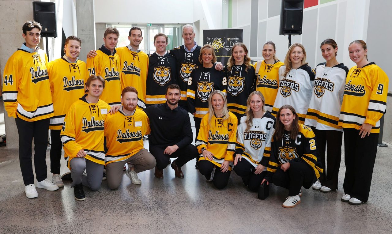 A group of people wearing black, white and gold hockey jerseys grouped together, smiling.