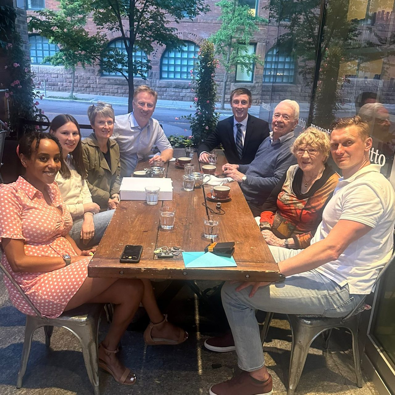 A group of people sitting at an outdoor table in a courtyard with glasses of water and tea cups after dinner.