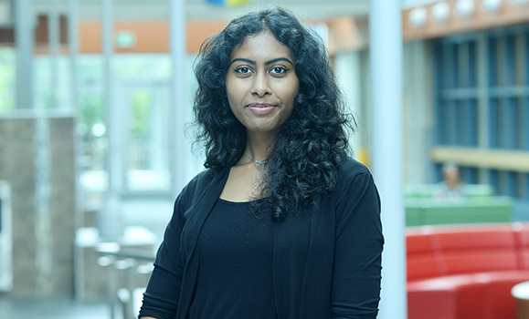 A woman wearing a black t-shirt and sweater faces the camera