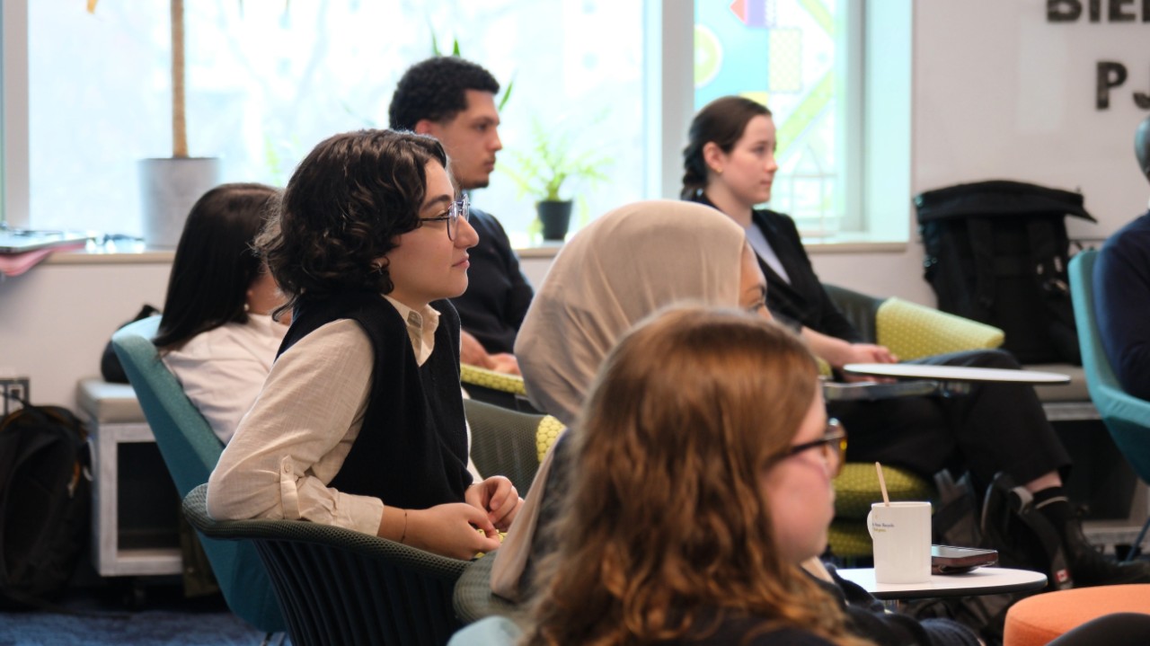 A group of students is seated in a casual classroom set-up focused on the teaching.
