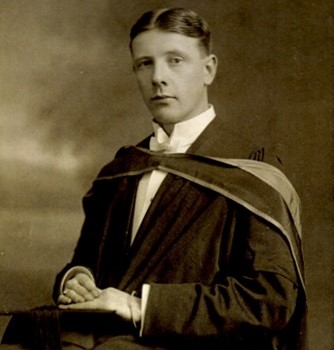 A black and white photo of a seated man wearing graduation robes
