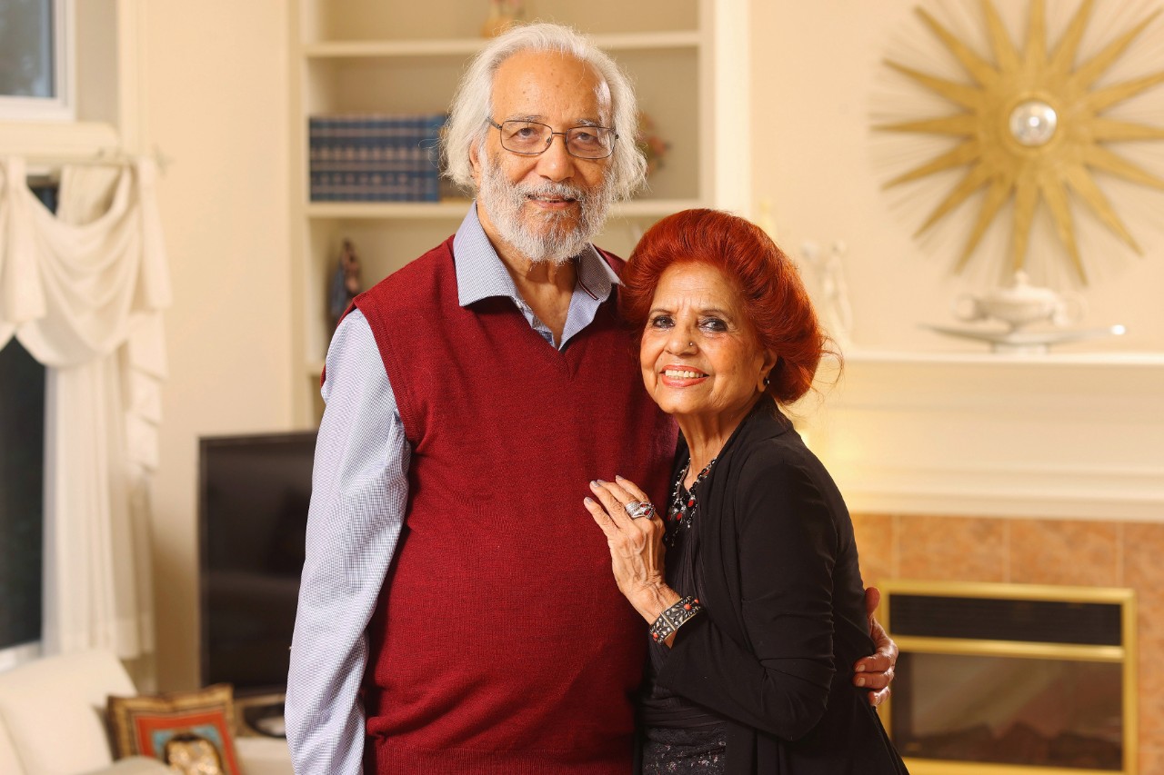A man wearing a red sweater vest embraces a woman wearing a black sweater