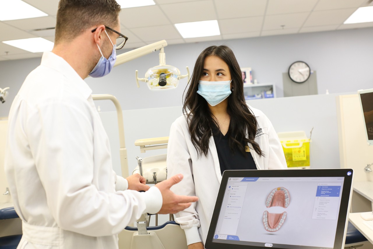 Two people in white lab coats and masks have a discussion in a dental clinic