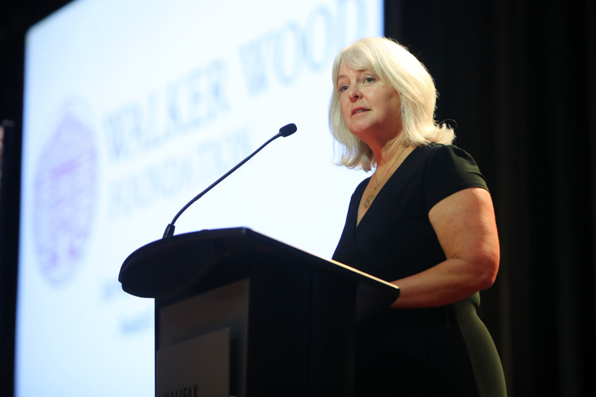 A woman wearing a black dress addresses the crowd from a podium