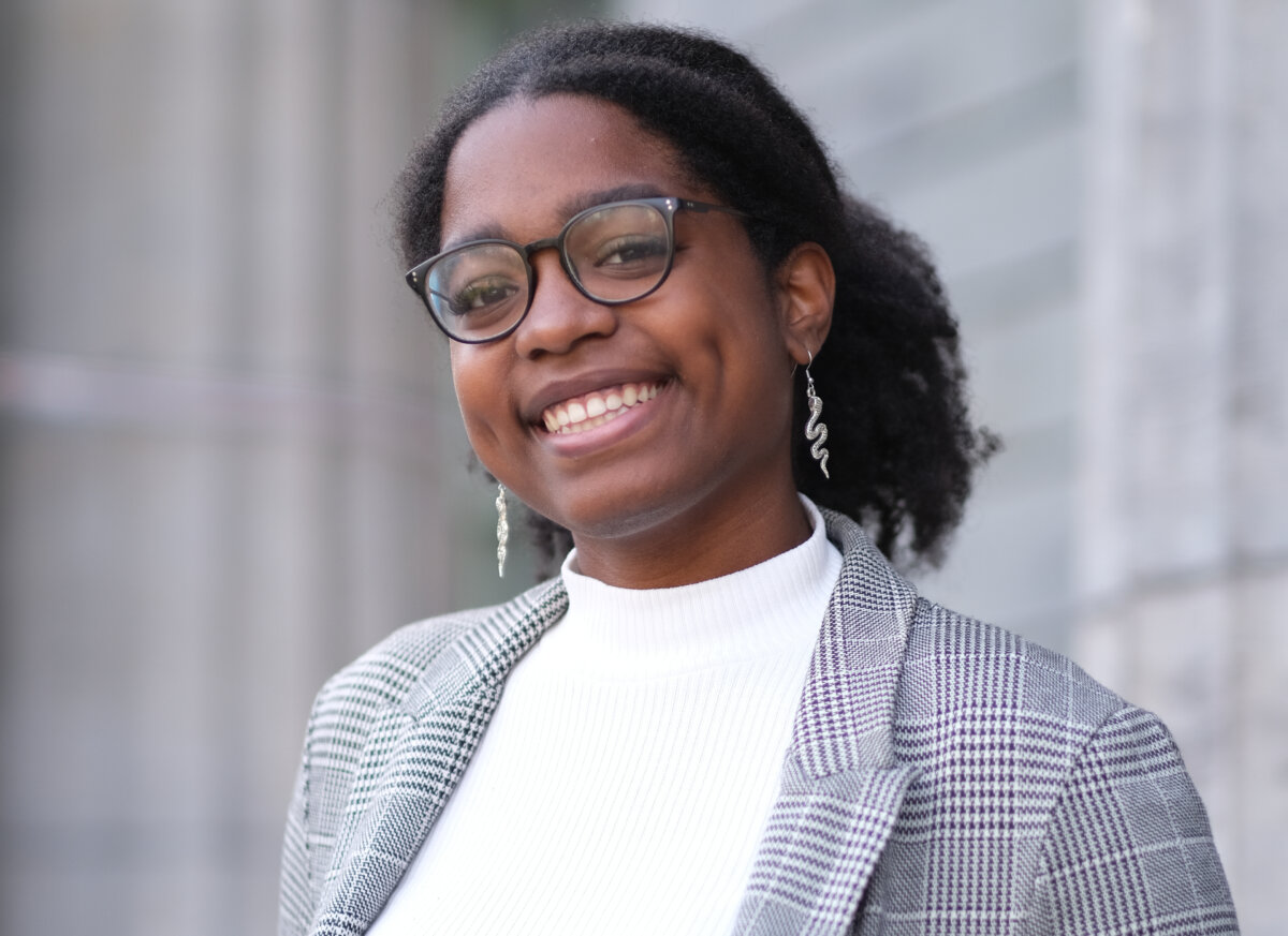 A woman wearing a grey suit jack and white blouse stands outside of a building
