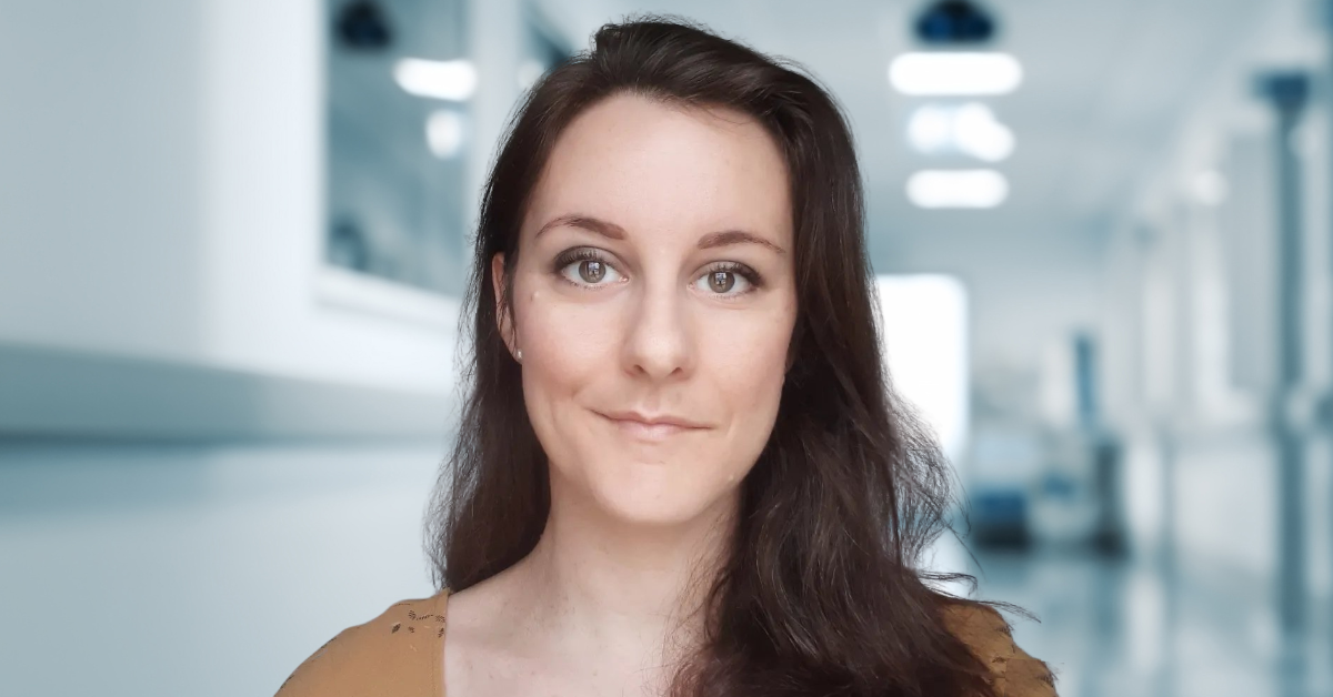 A woman with long brown hair stands in a hospital hallway