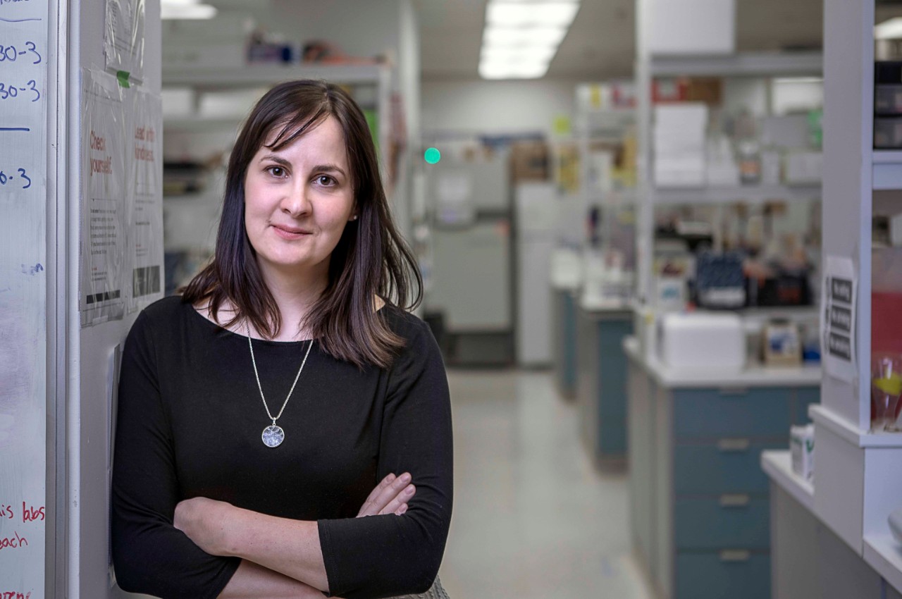 A woman with brown hair leans against a wall with her arms crossed