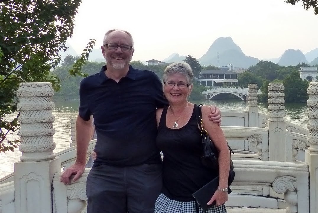 A couple standing together outdoors while on vacation overlooking a body of water.