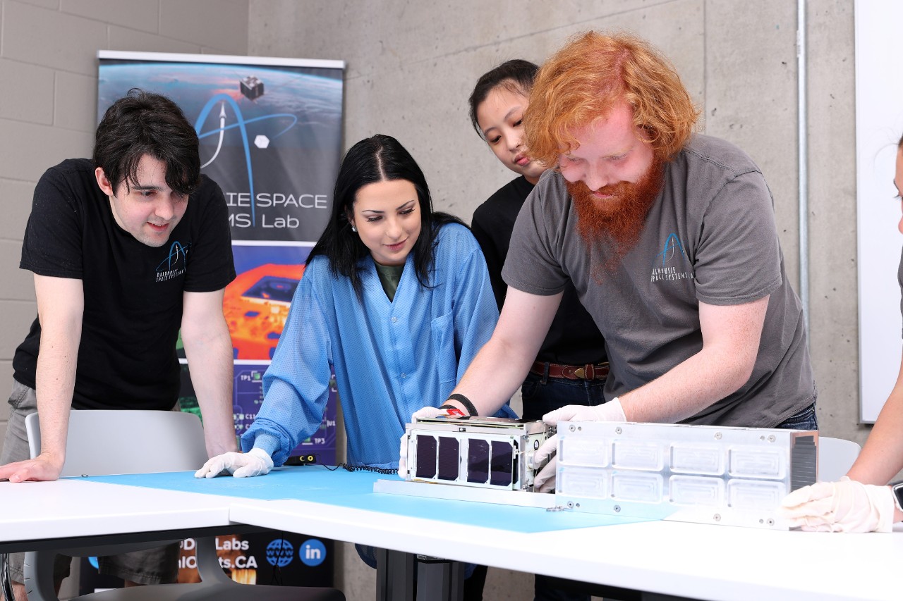 Four people gather around equipment on a table during a presentation.