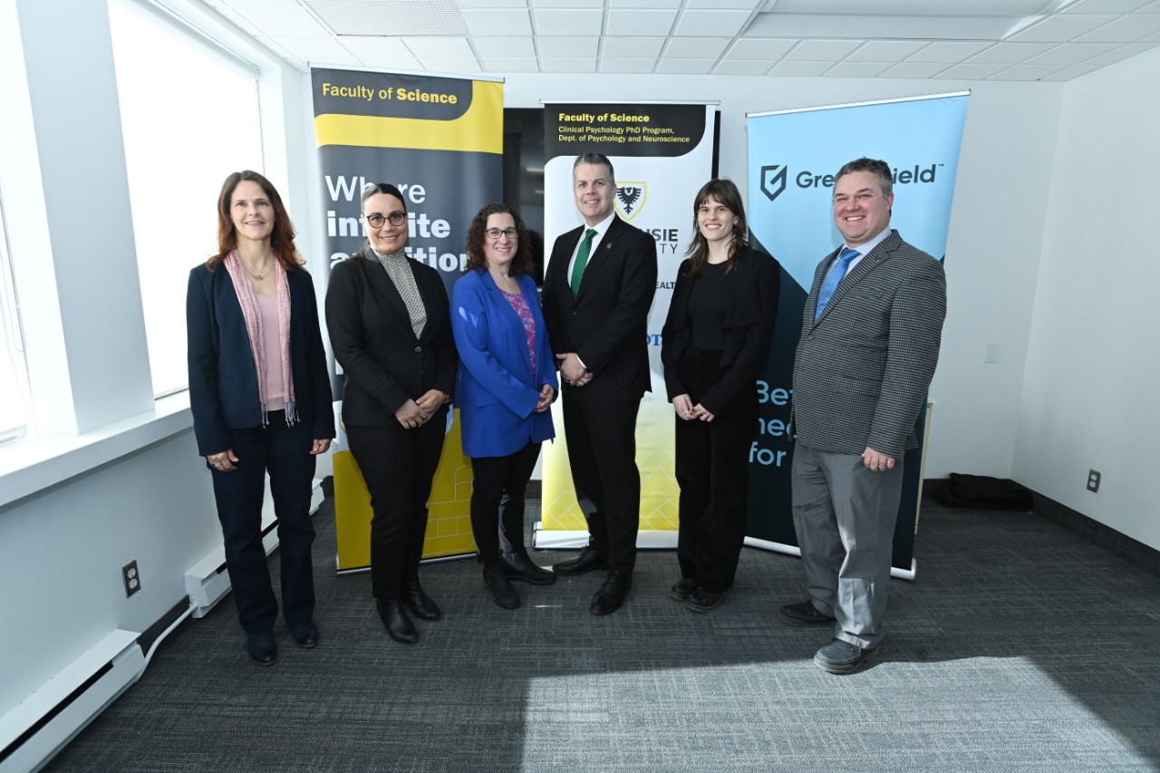 A group of six people wearing suits stand in front of three pop up banners.
