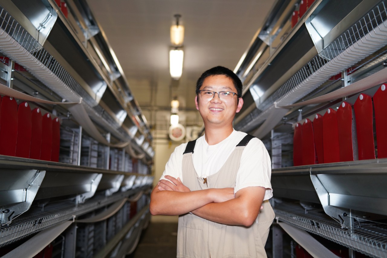 Xujie Li smiling between rows of shelving.