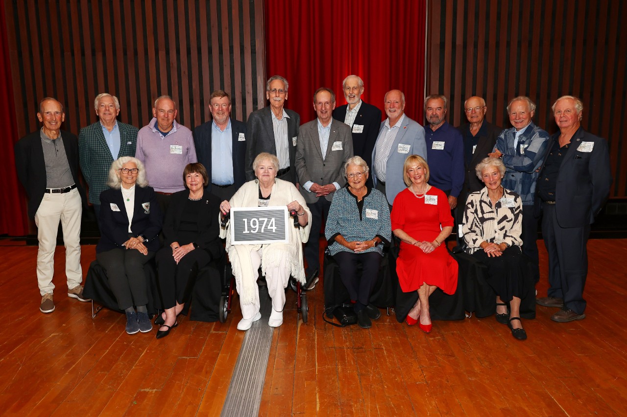 A group of alumni from the law class of 1974 stand in the back row behind a seated front row while attending an event.