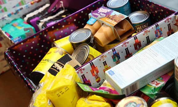 Non-perishable food items and toiletry items in boxes with holiday wrapping.