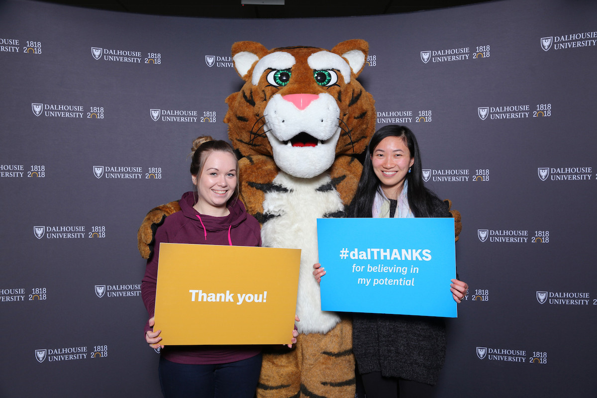 Two women holding signs that day thank you pose with the tiger mascot