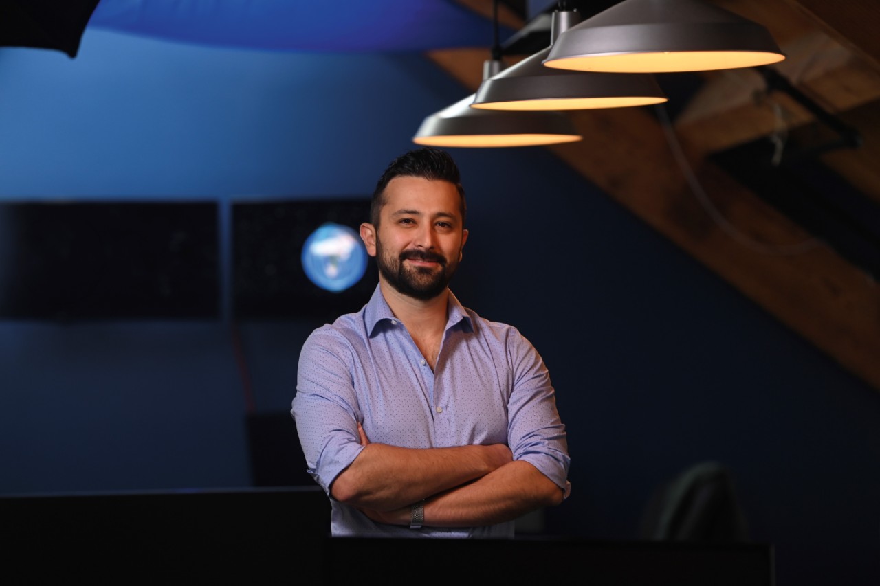 A man wearing a blue button-up shirt stands with his arms crossed