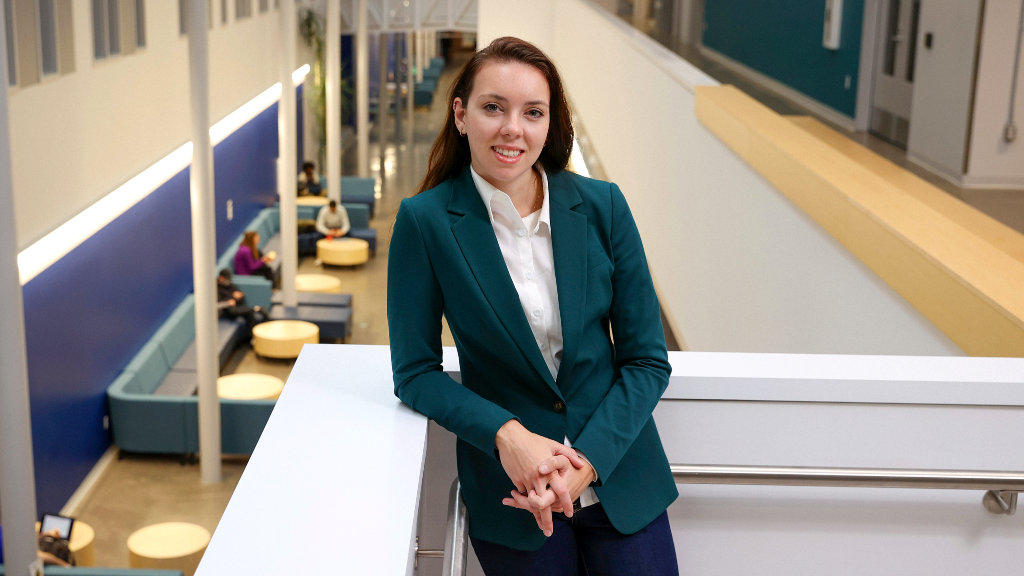 A woman wearing a green blazer and jeans leaning against a ledge on the second floor of an atrium