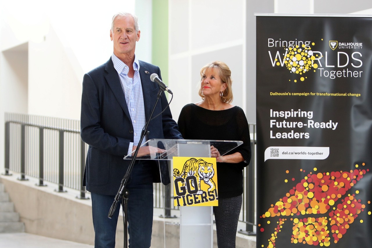 McCain speaks into a microphone at a podium during an event while McLean looks up at him by his side.