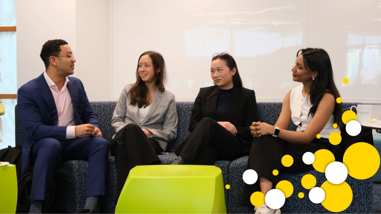 A diverse set of four students is engaged in conversation seated on a couch and dressed in business casual attire. 