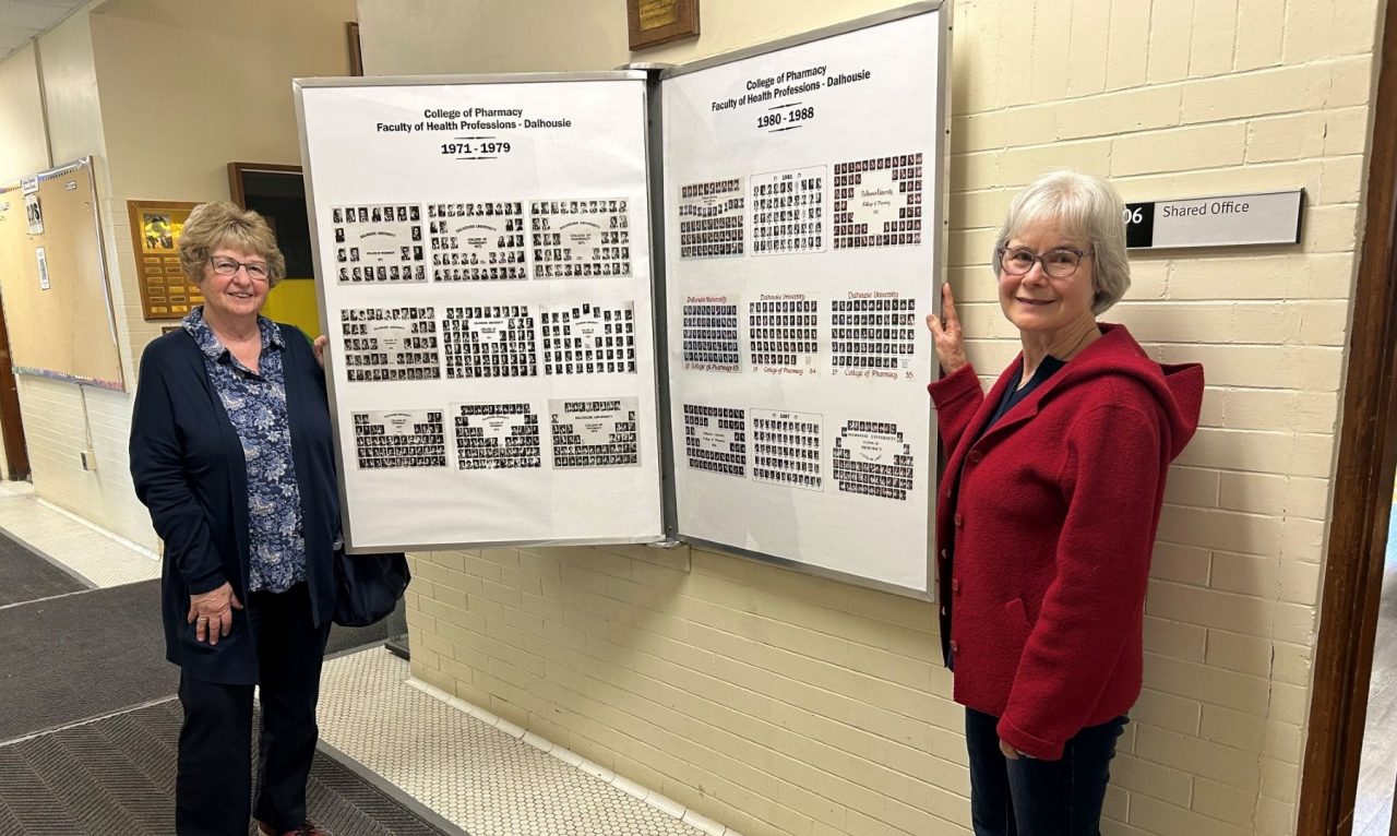 Two women stand on either side of a display of composite grad photos.