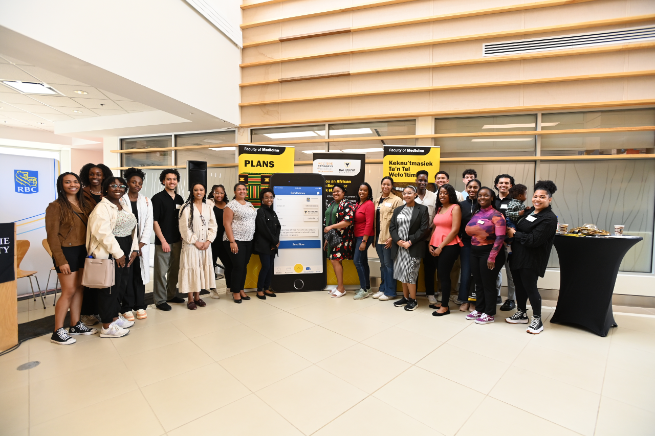 A large group of people pose around a display board shaped like a large iphone.