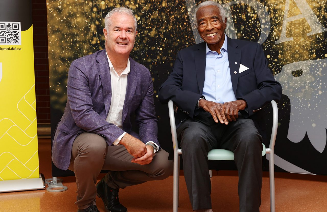 A man crouches next to another man seated in a chair