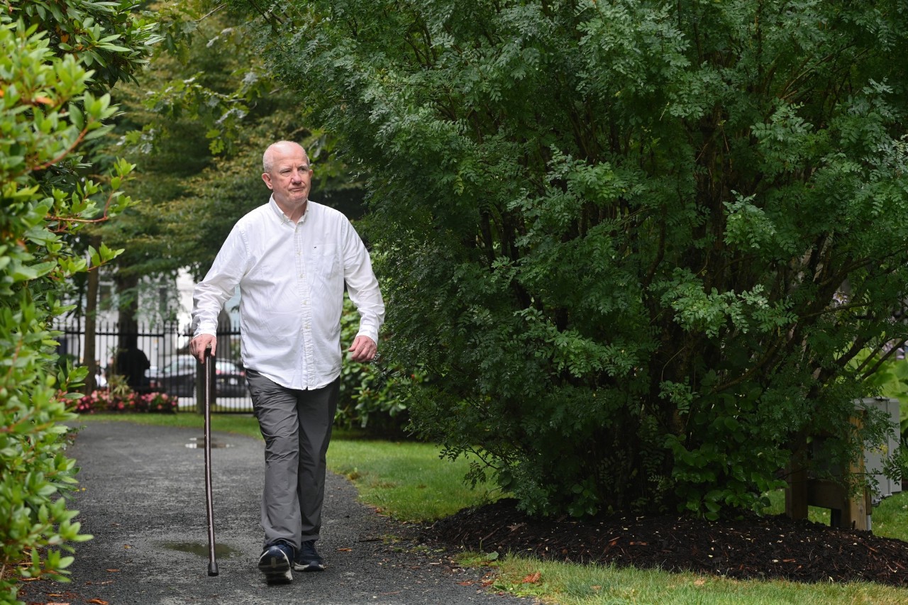 A man walking with a cane along a treed path in summer.