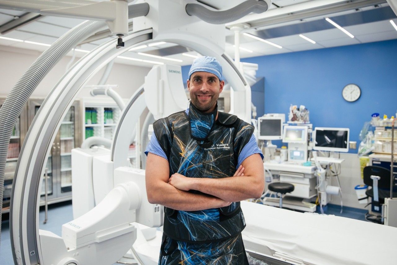 Volders standing with arms crossed, smiling in a medical exam room in front of medical equipment and machines.