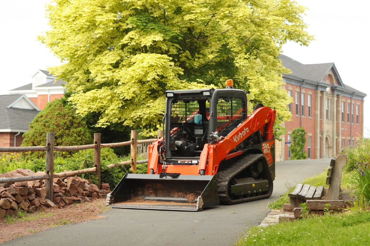Agricultural machine on a laneway outside a university building in summer.