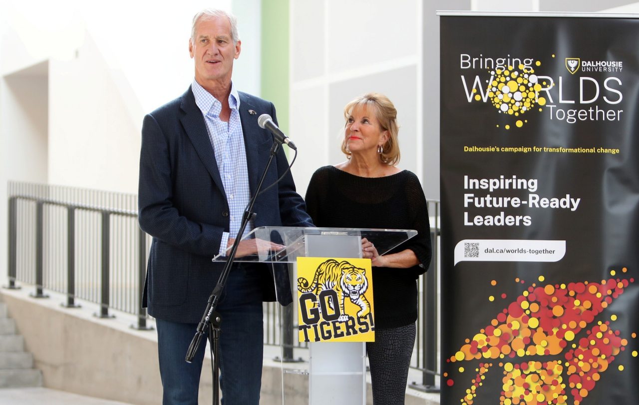 McCain speaks into a microphone at a podium during an event while McLean looks up at him by his side.