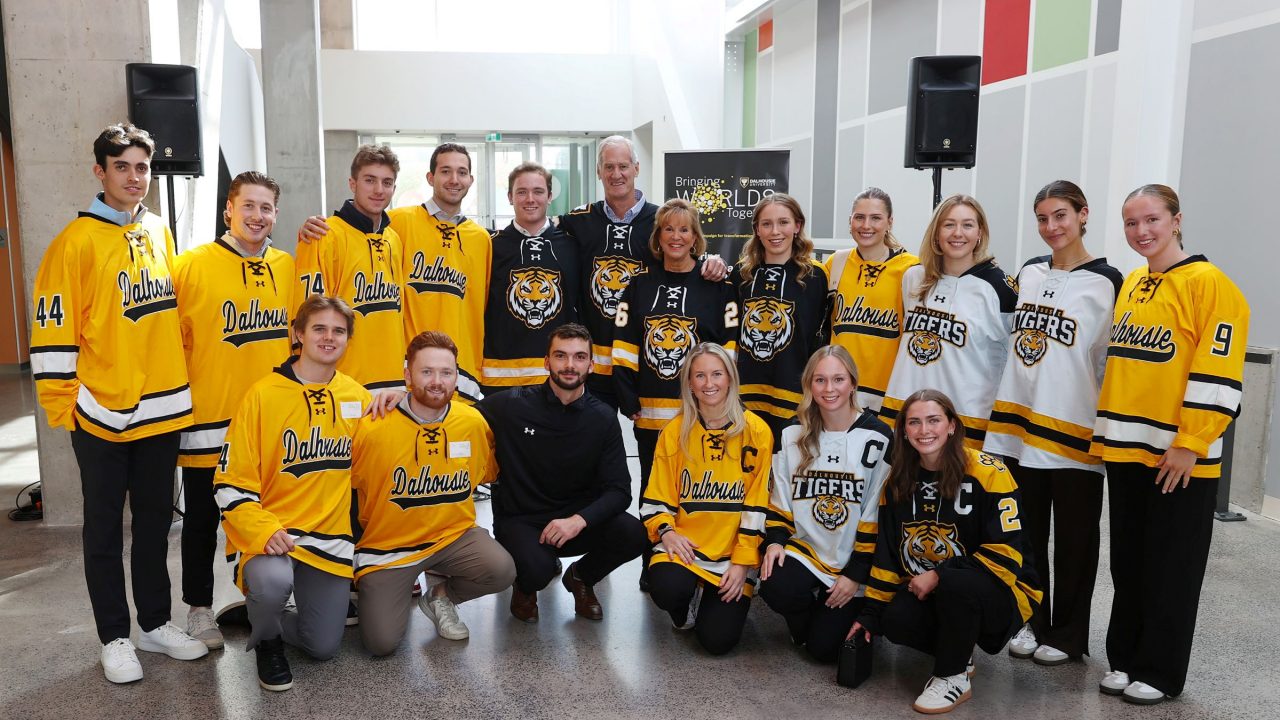 A group of people wearing black, white and gold hockey jerseys grouped together, smiling.