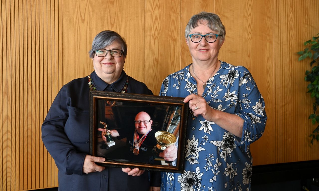 Two women hold a framed photo of their brother.