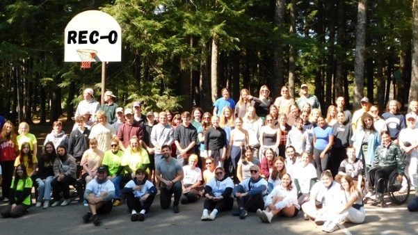 A large group of people gathered outdoors with tall trees in the background.