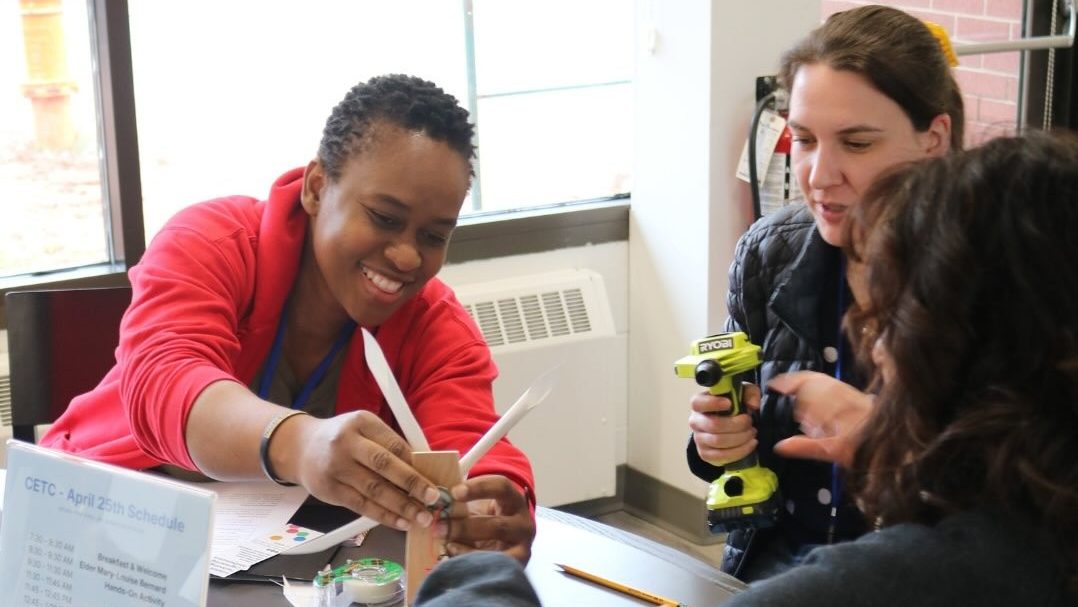 A younger student is sitting at a table working with two others to build a scientific model.