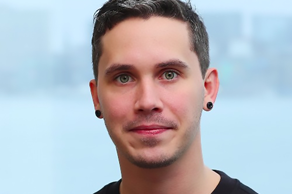 A man with lightly grey hair faces the camera wearing a black t-shirt