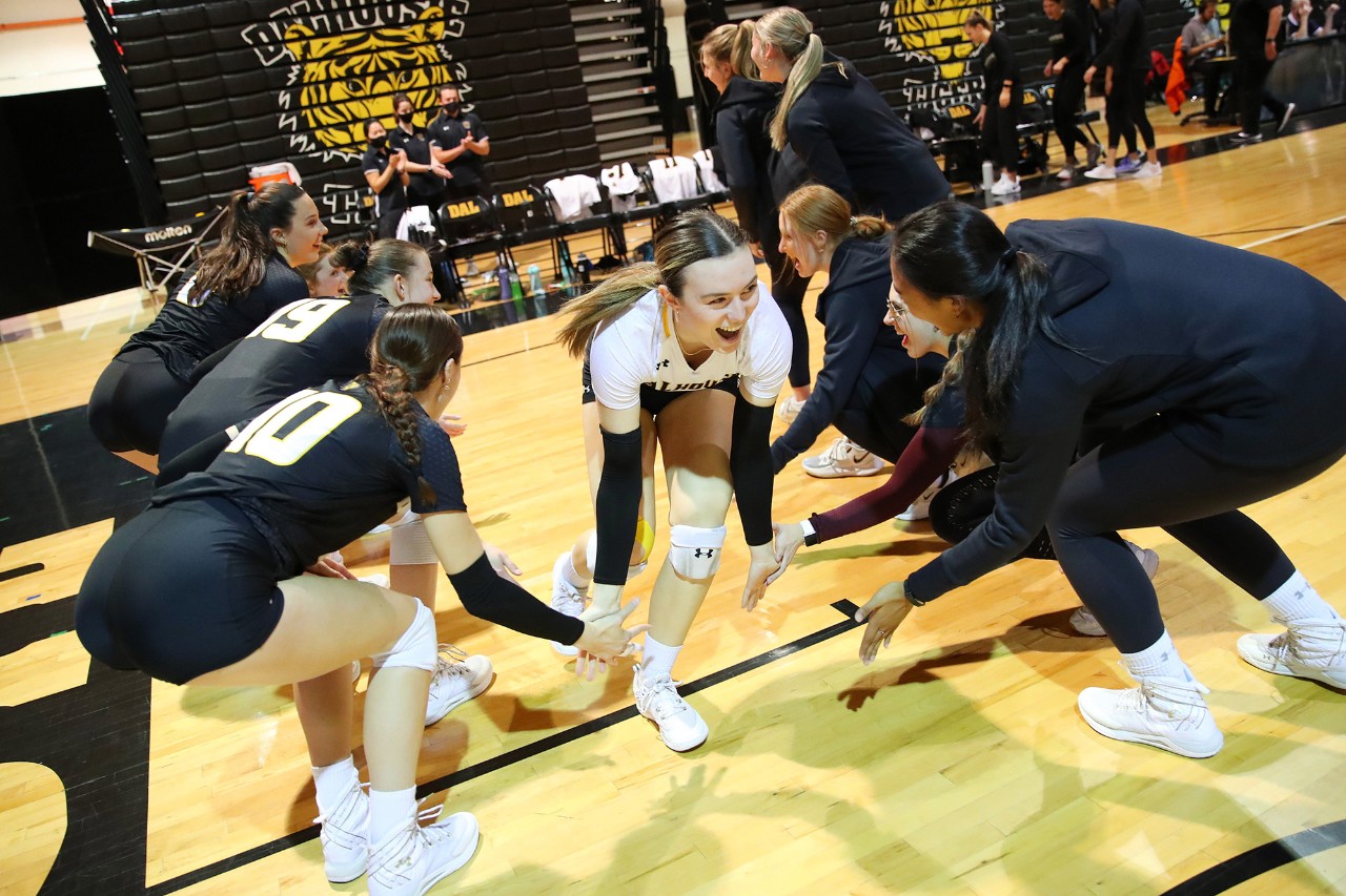 Women's volleyball team dressed in black and gold uniforms giving each other high fives.
