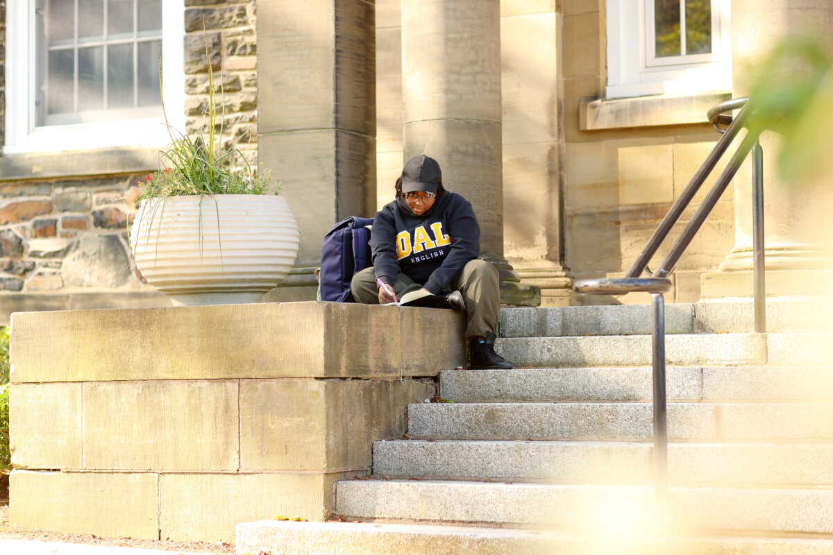 A woman sitting on a stone stairwell writes in a notebook