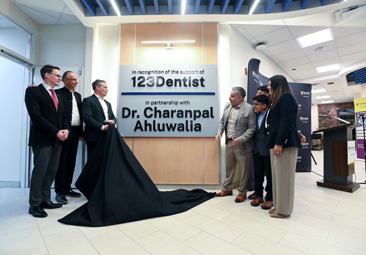 Several people stand on either side of commemorative signage on the wall in a building lobby with a black curtain having been removed.