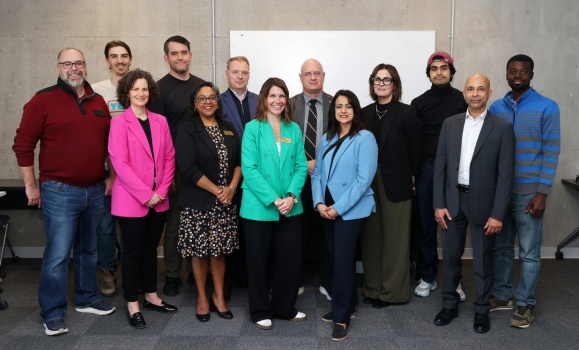 A group of people stand together in a classroom space at a celebration.