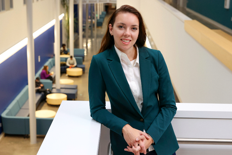 A woman wearing a green blazer and jeans leaning against a ledge on the second floor of an atrium