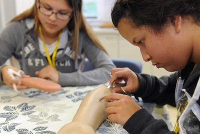 Two students seated at a table practicing a medical procedure on plastic arms 