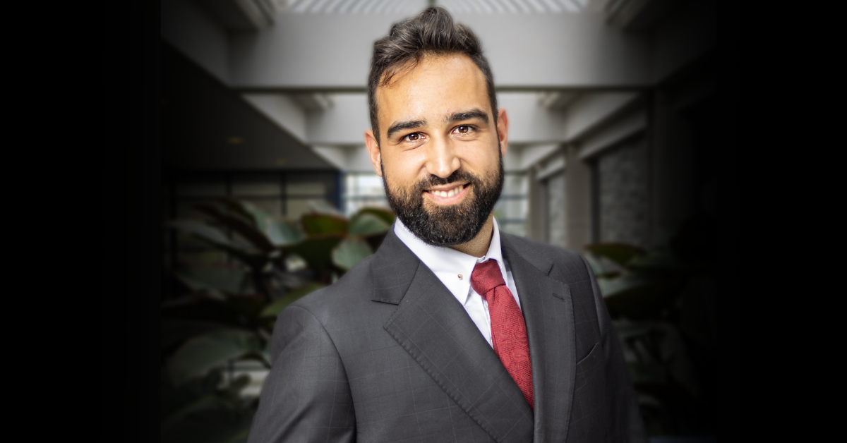 A headshot of a man wearing a grey suit and red tie 
