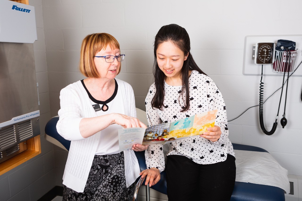 A staff member of Dalhousie's Student Health & Wellness centre consults a brochure with a student in a clinician's room.
