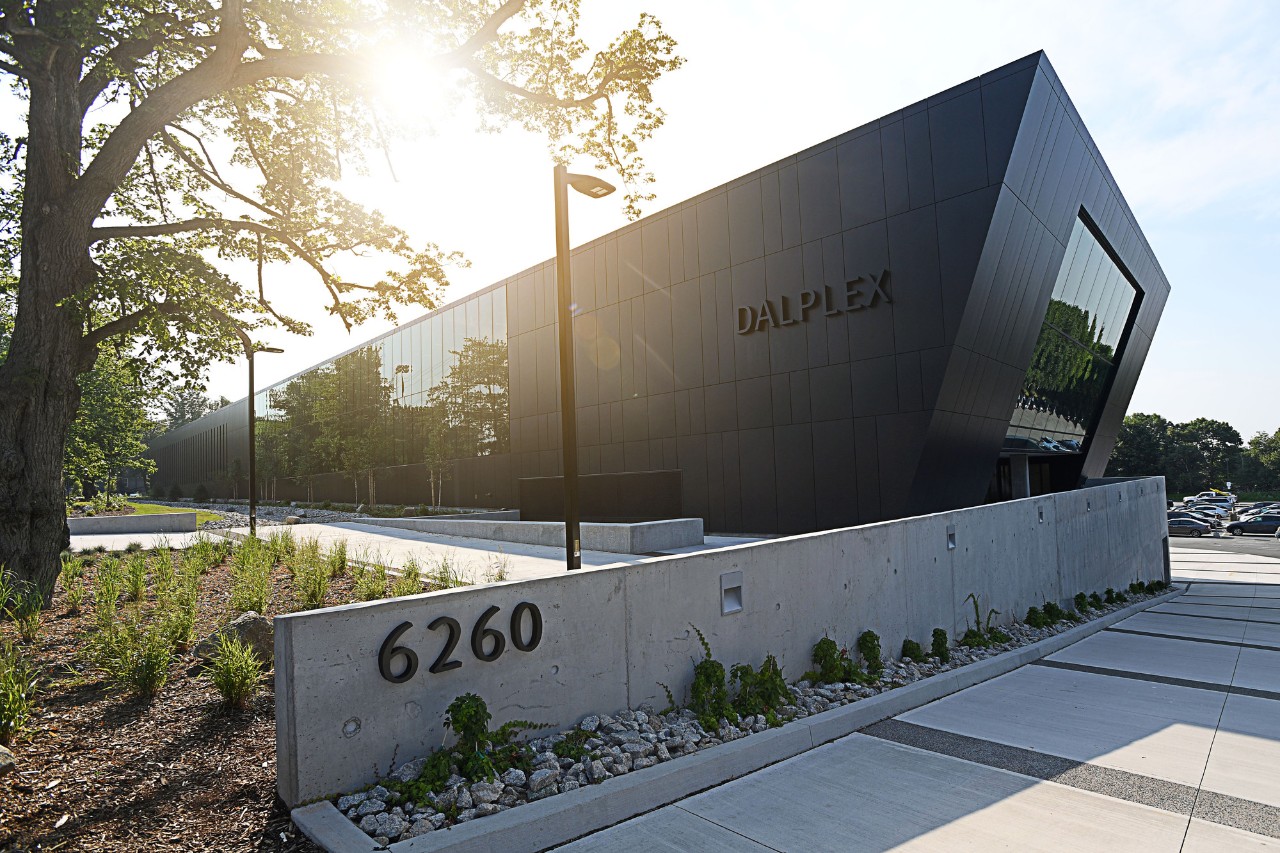 The sun shines behind a geometric black building with windows and the word DALPLEX on the side. 