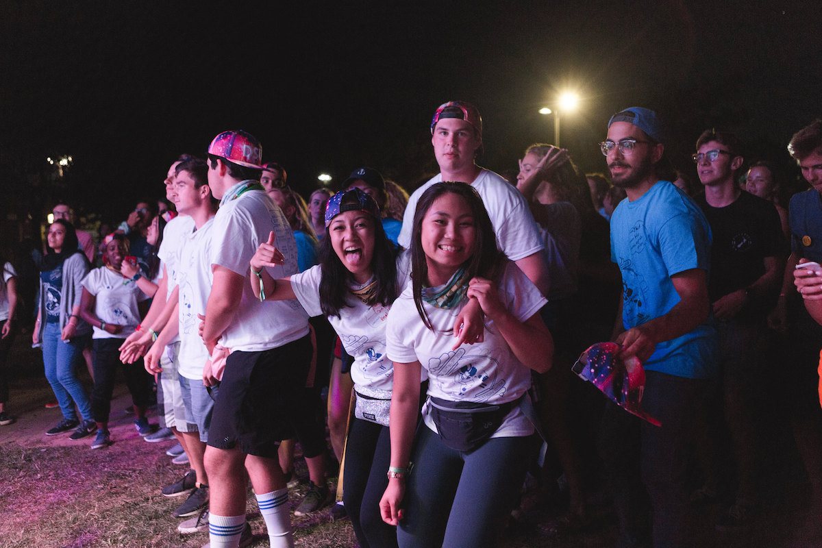 A group of university students stand outside and smile to the camera at night.