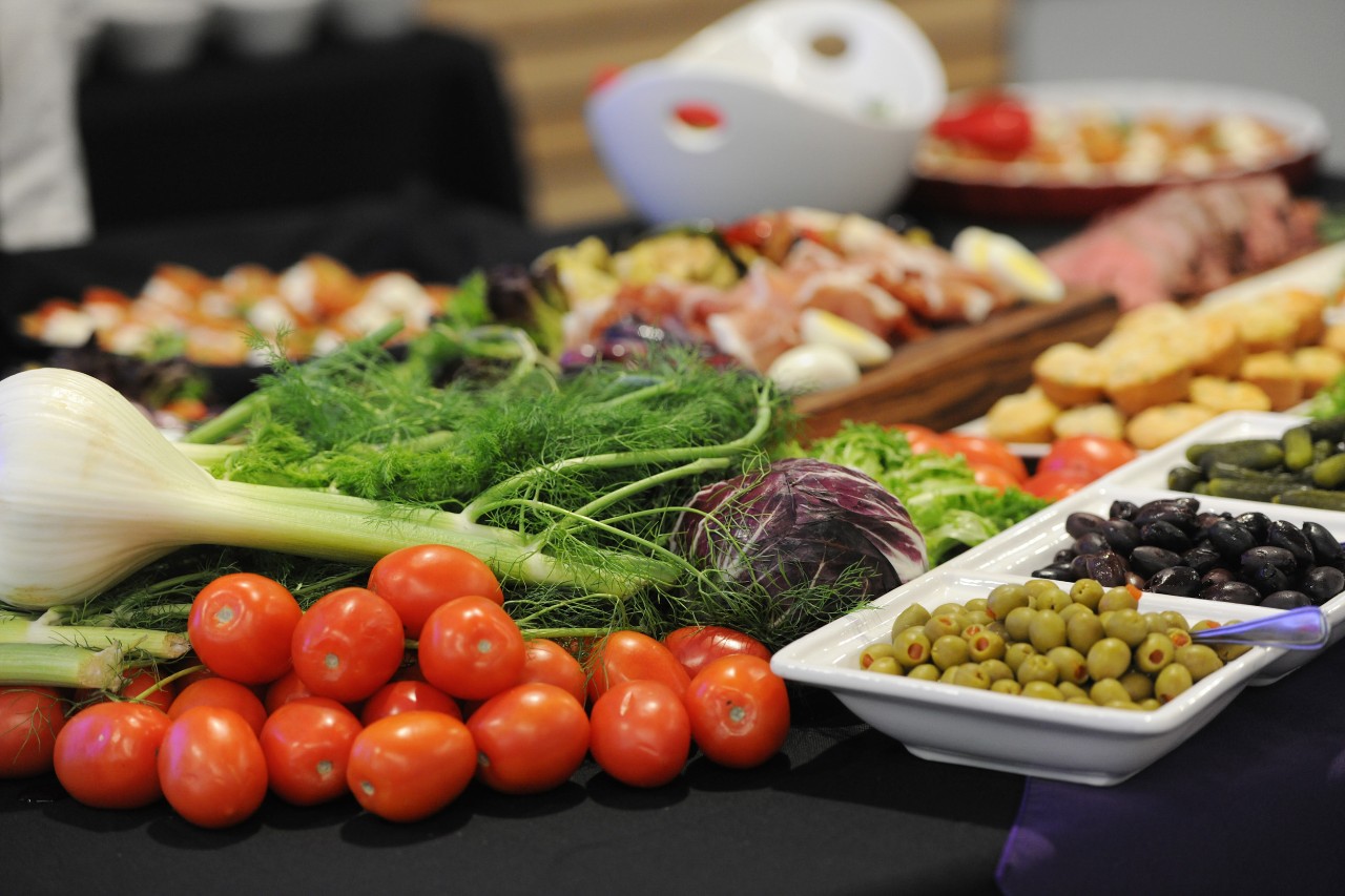 A spread of brightly coloured fruits and vegetables and appetizers is on a table at an event