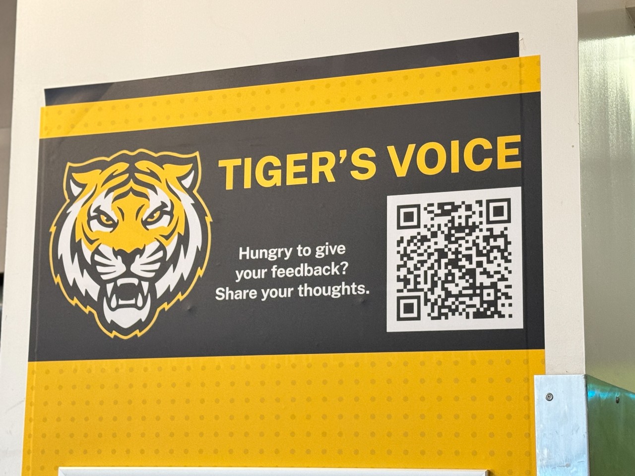 A sign for the Tigers Voice survey hangs above the bulleting board with a QR Code encouraging students to share feedback