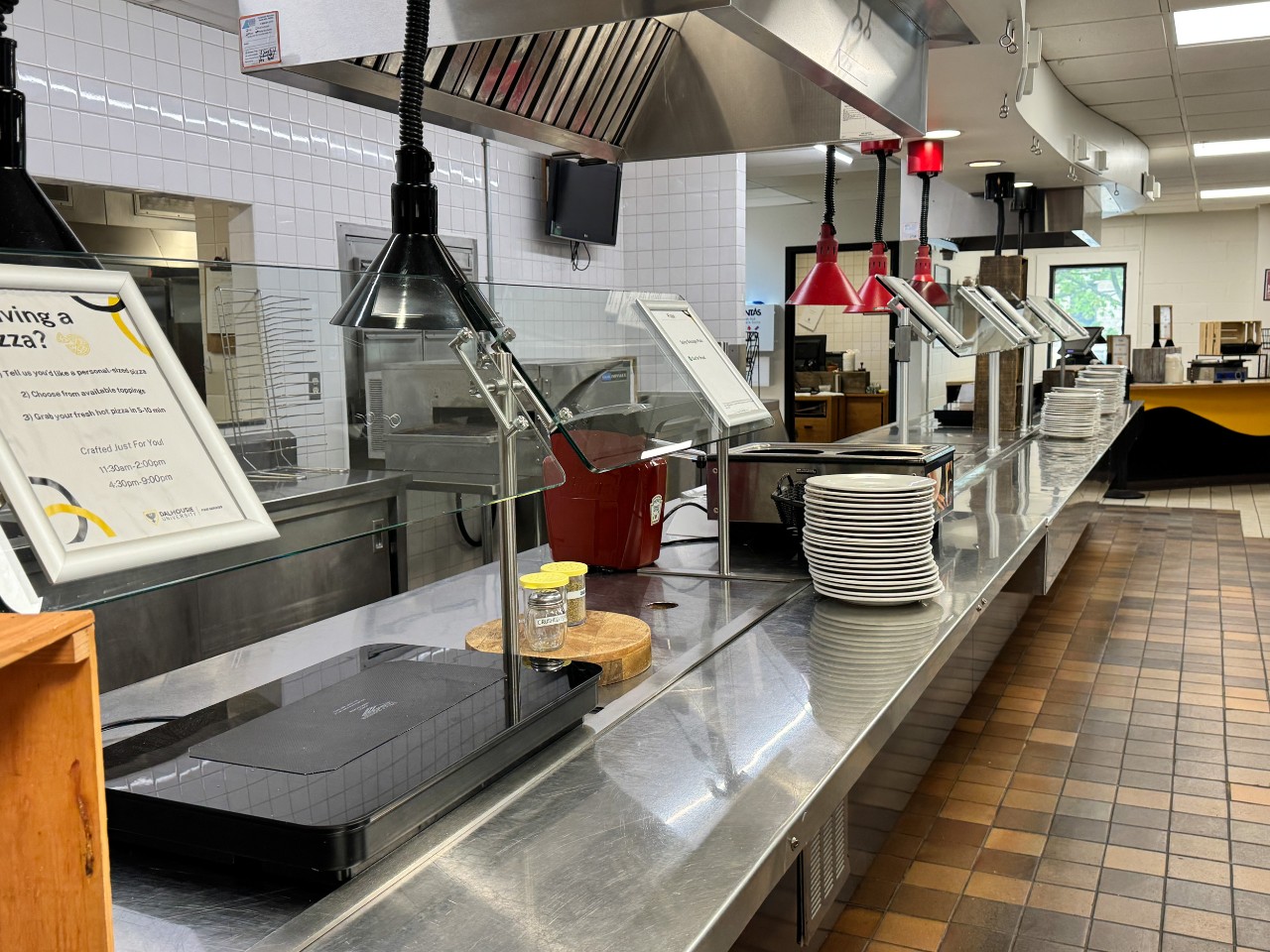 The stainless steel serving counter has stacks of plates ready for students to enjoy hot meals
