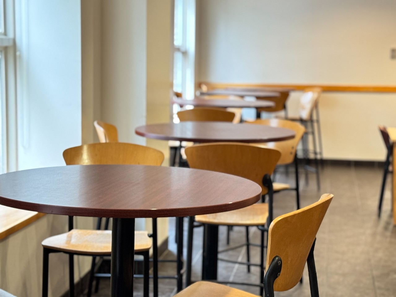 Tall round tables sit by the windows of the dining hall